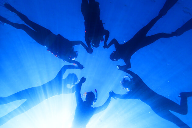 水面で6人で輪になっているシュノーケラーを水中から見上げている画像